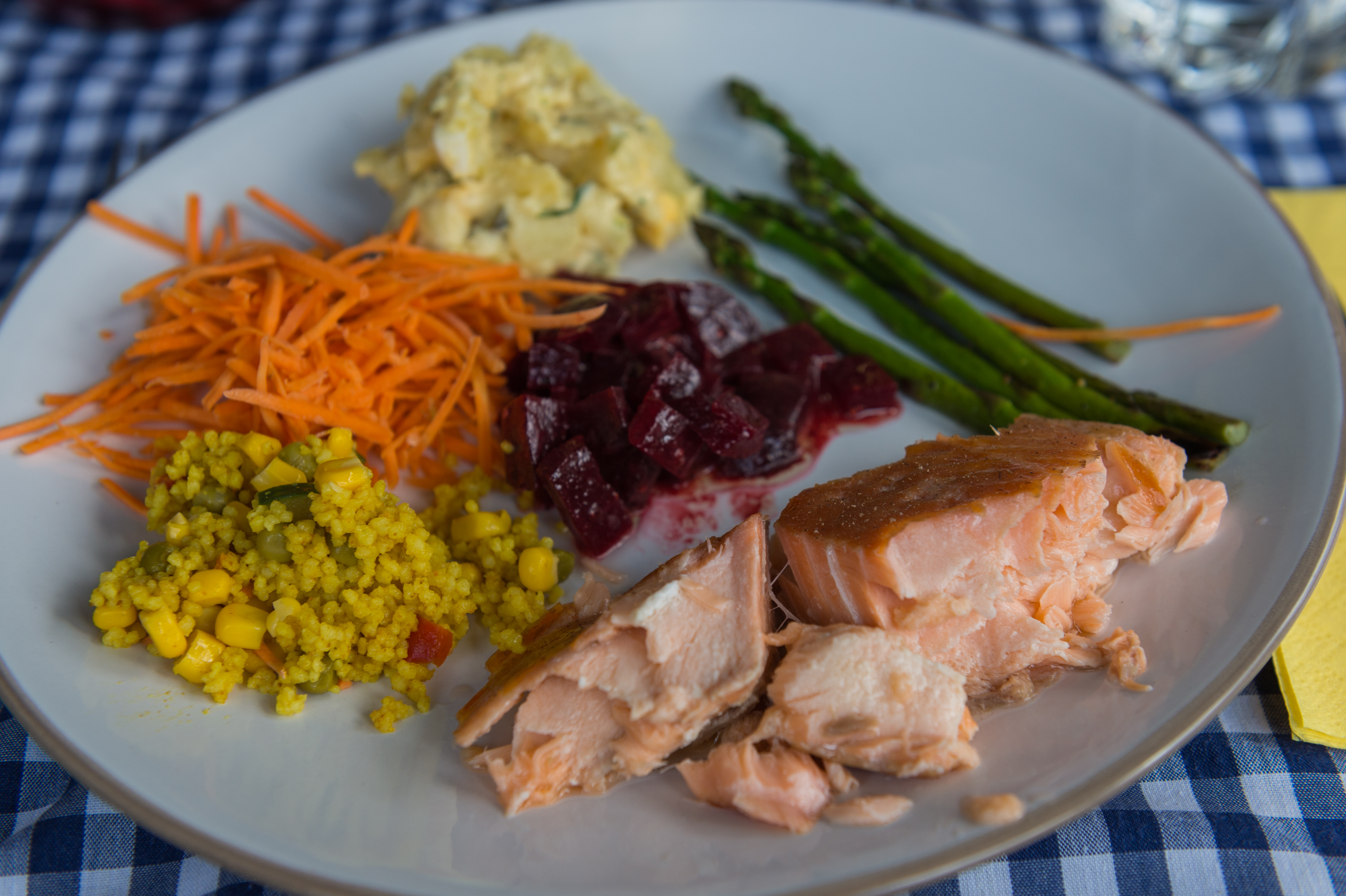 A plate of smoked salmon with asparagus, beet salad, shredded carrots, potato salad, and yellow couscous on a table.