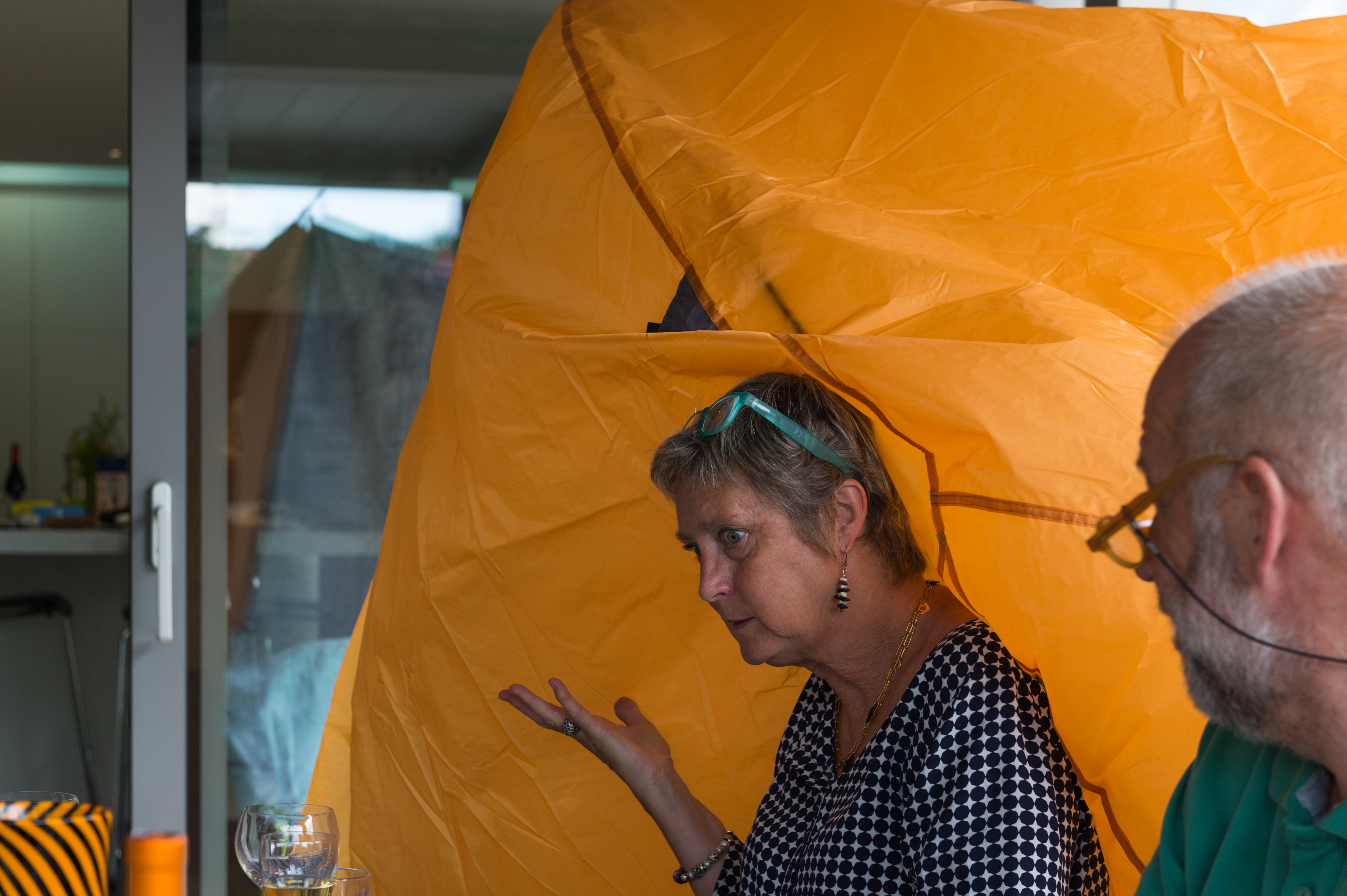 A woman sits with part of a yellow tent draped over her head, gesturing while talking to a man.