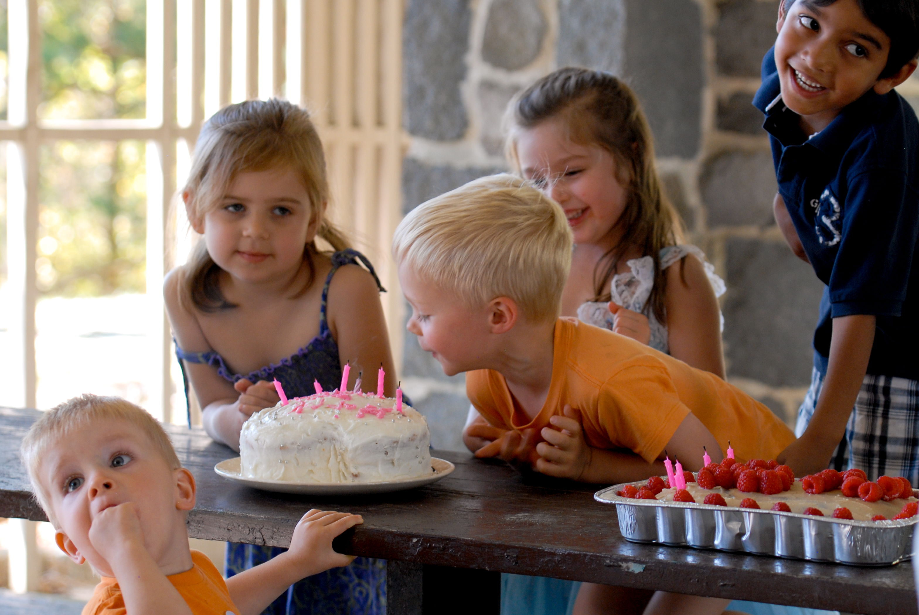 Children gather around a birthday cake with lit candles, laughing and excitedly preparing to celebrate.