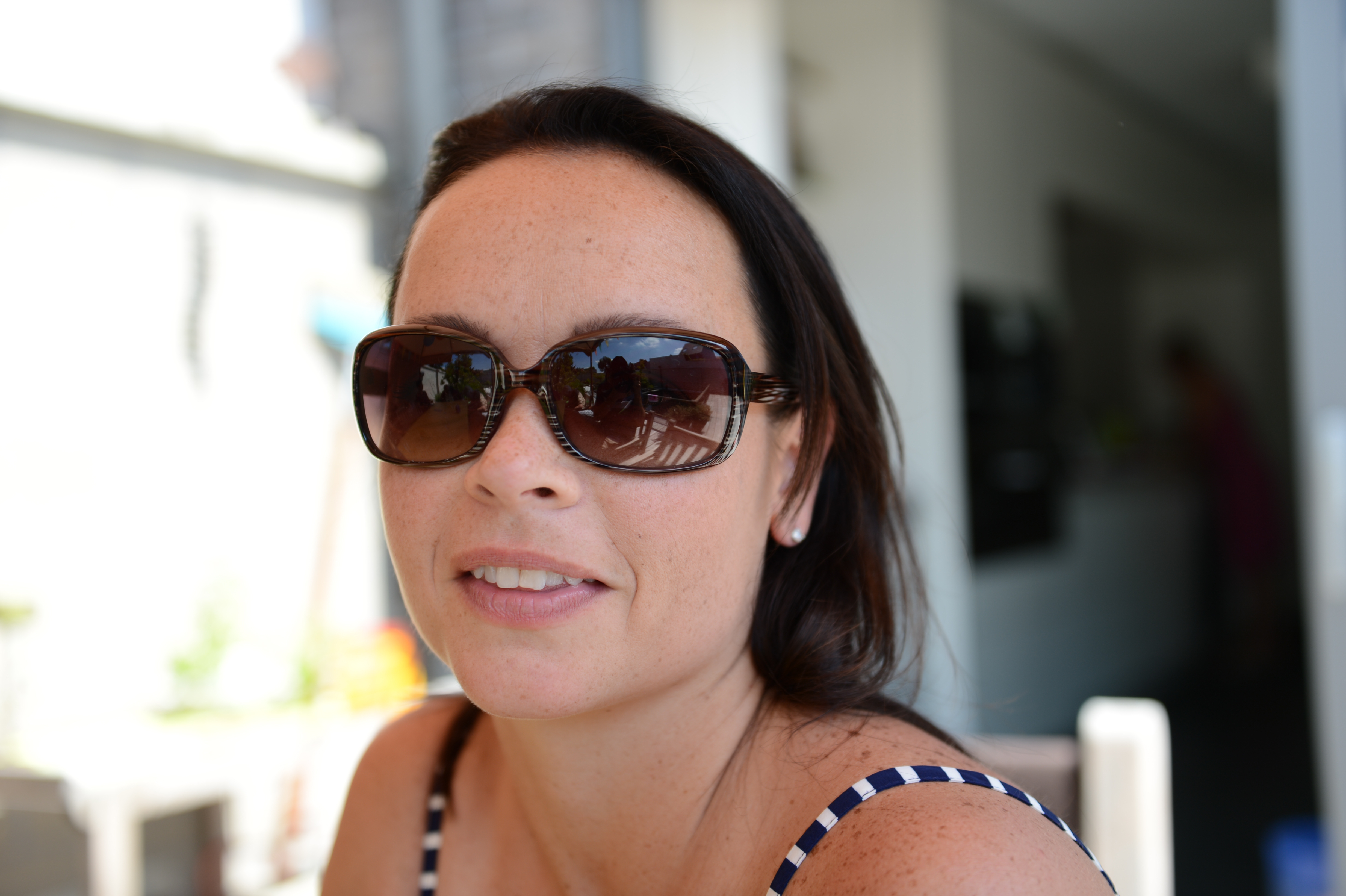 A woman wearing sunglasses and a striped top sits and smiles at the camera during a gathering.