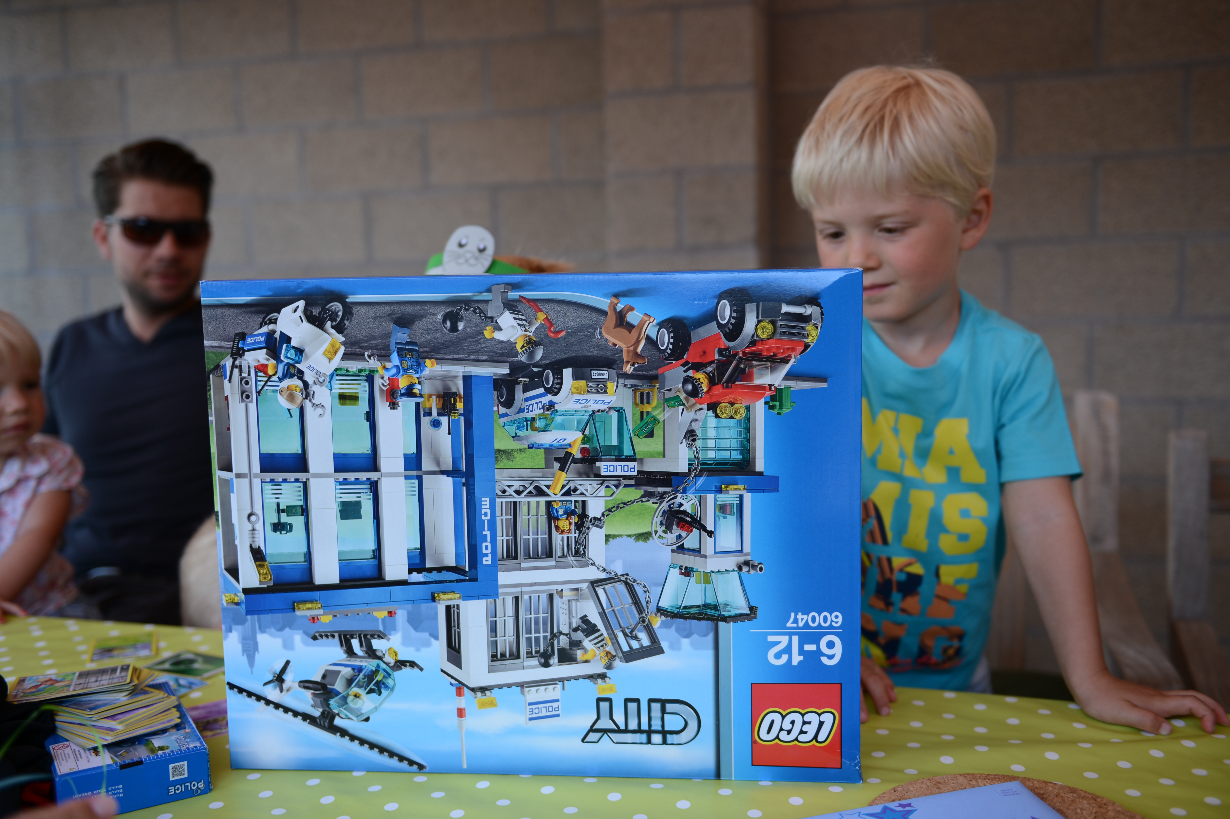 A young child in a blue shirt excitedly looks at a large LEGO City police set at a party.