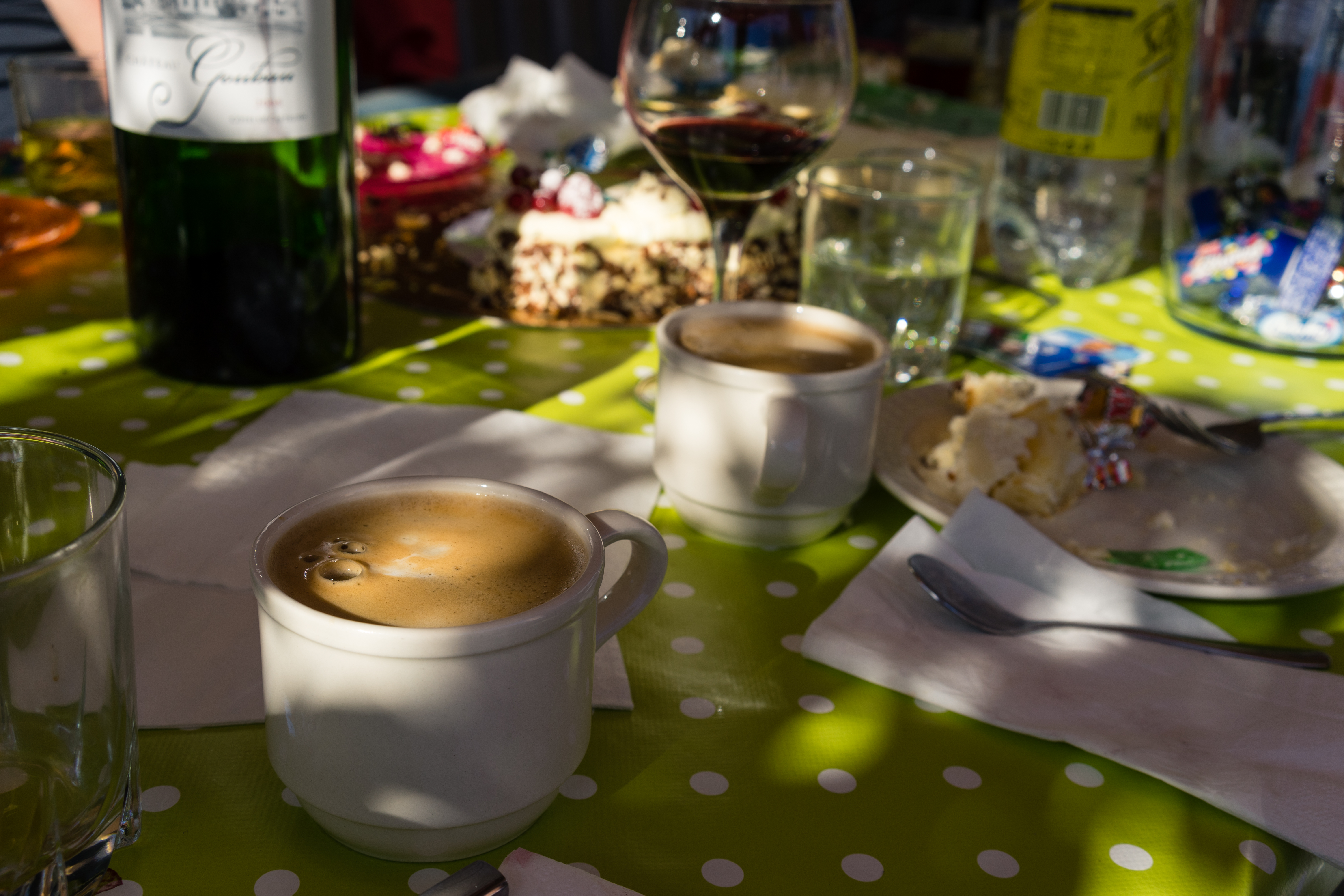 Two cups of coffee on a table with cake, wine, and other drinks after a party.
