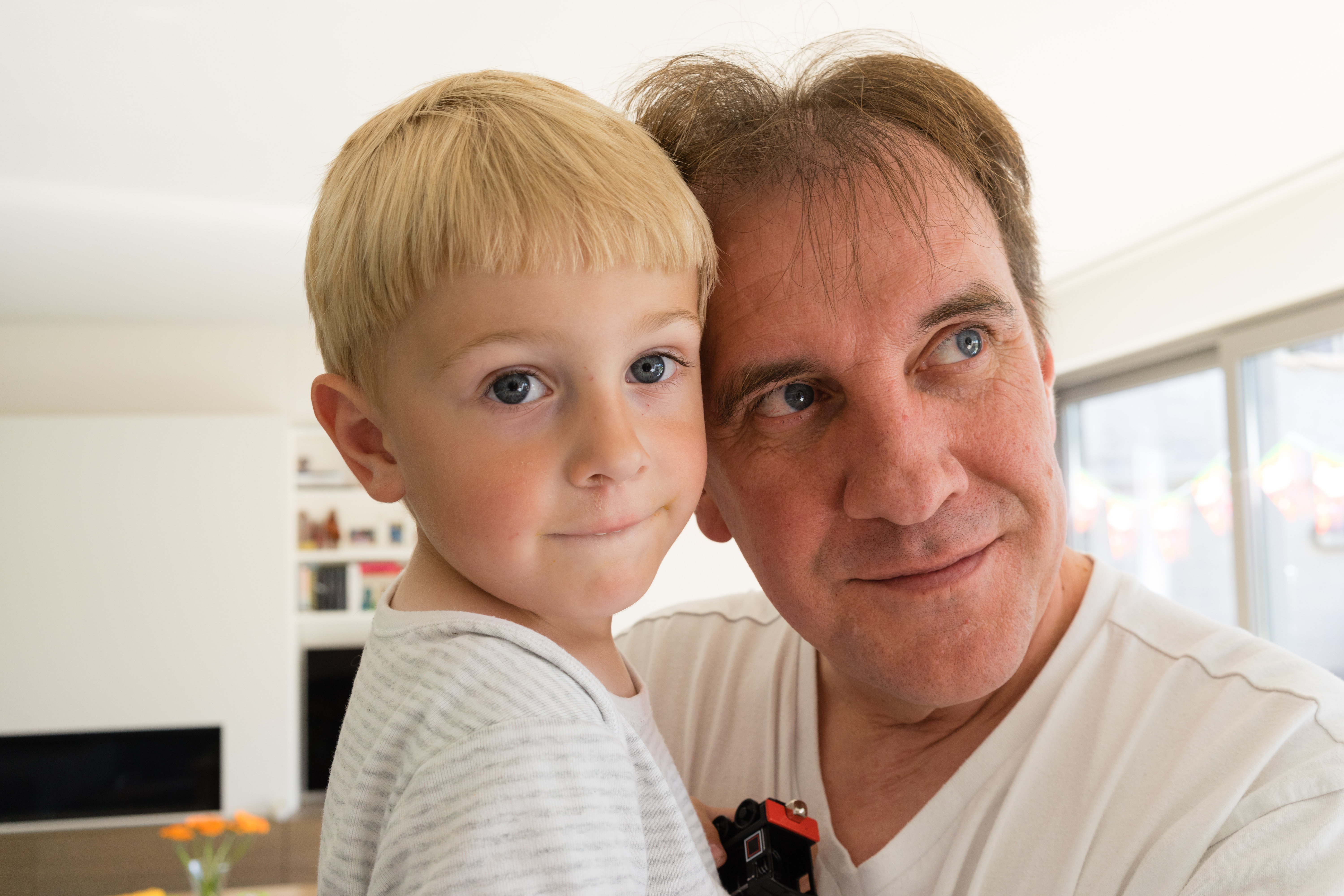 A man in a white shirt hugs a young child holding a small toy, both looking in different directions.