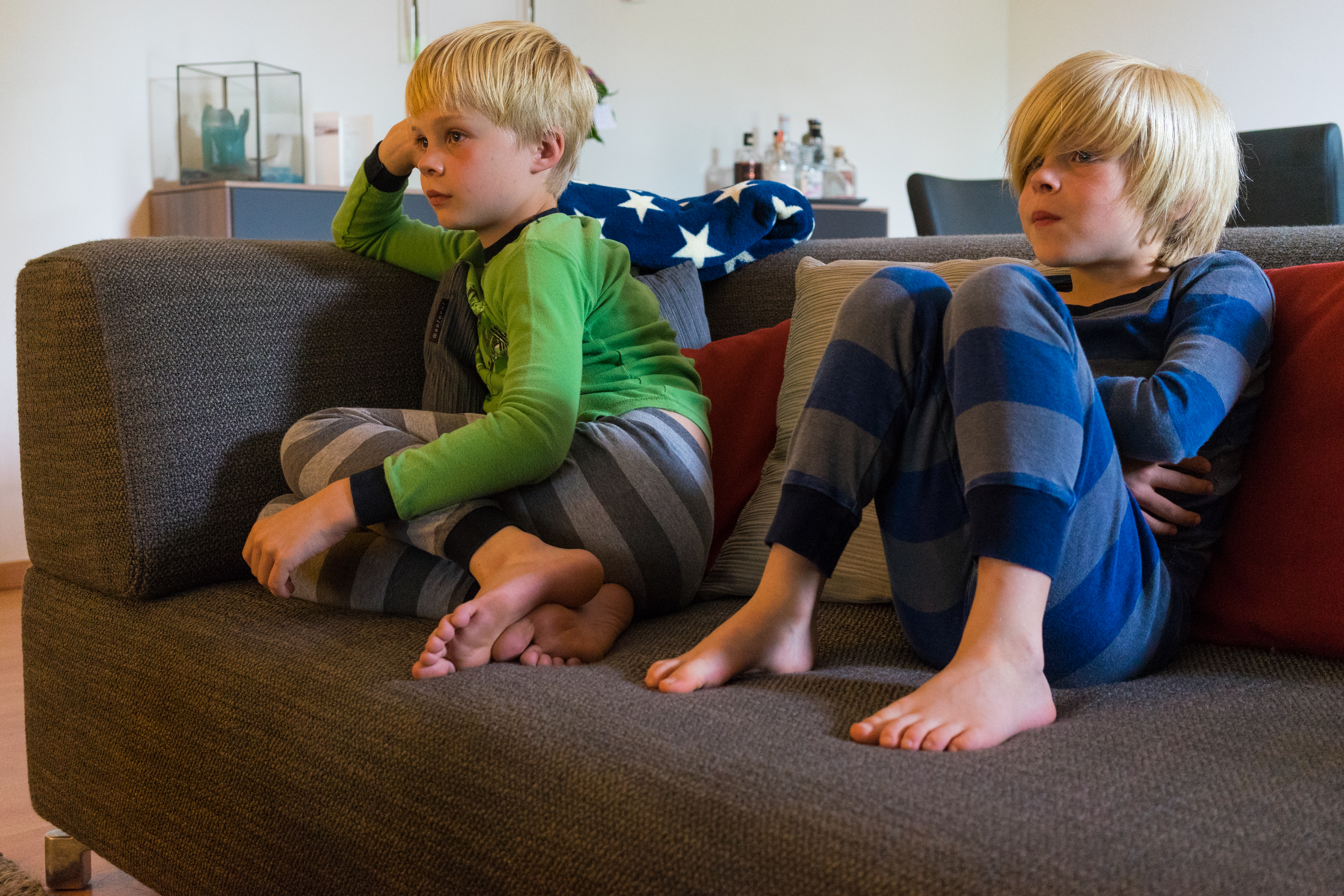 Two children in pajamas sit on a couch, watching something with focused expressions.