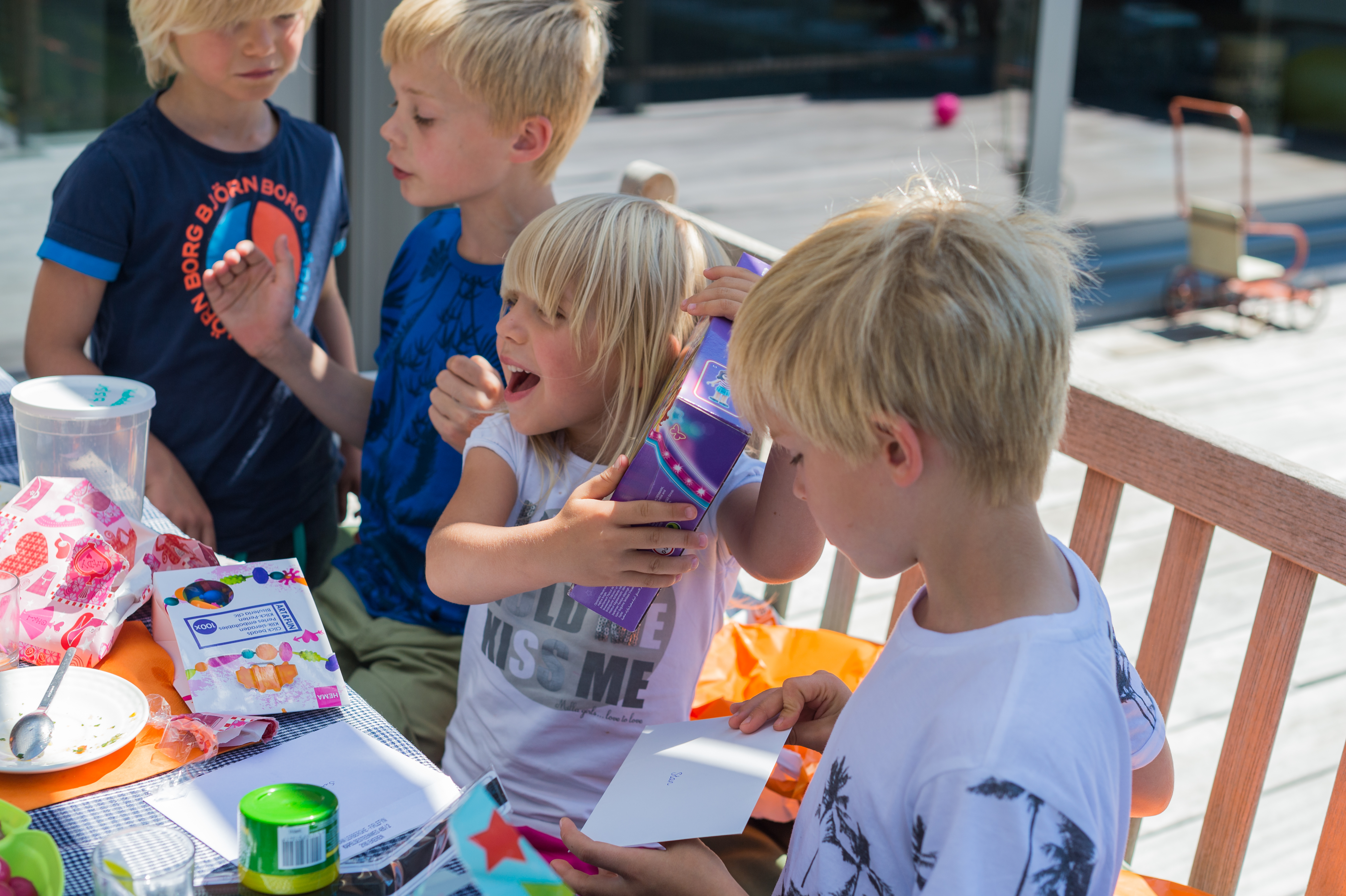 A child excitedly opens a gift while sitting at a table with other children during a birthday celebration.