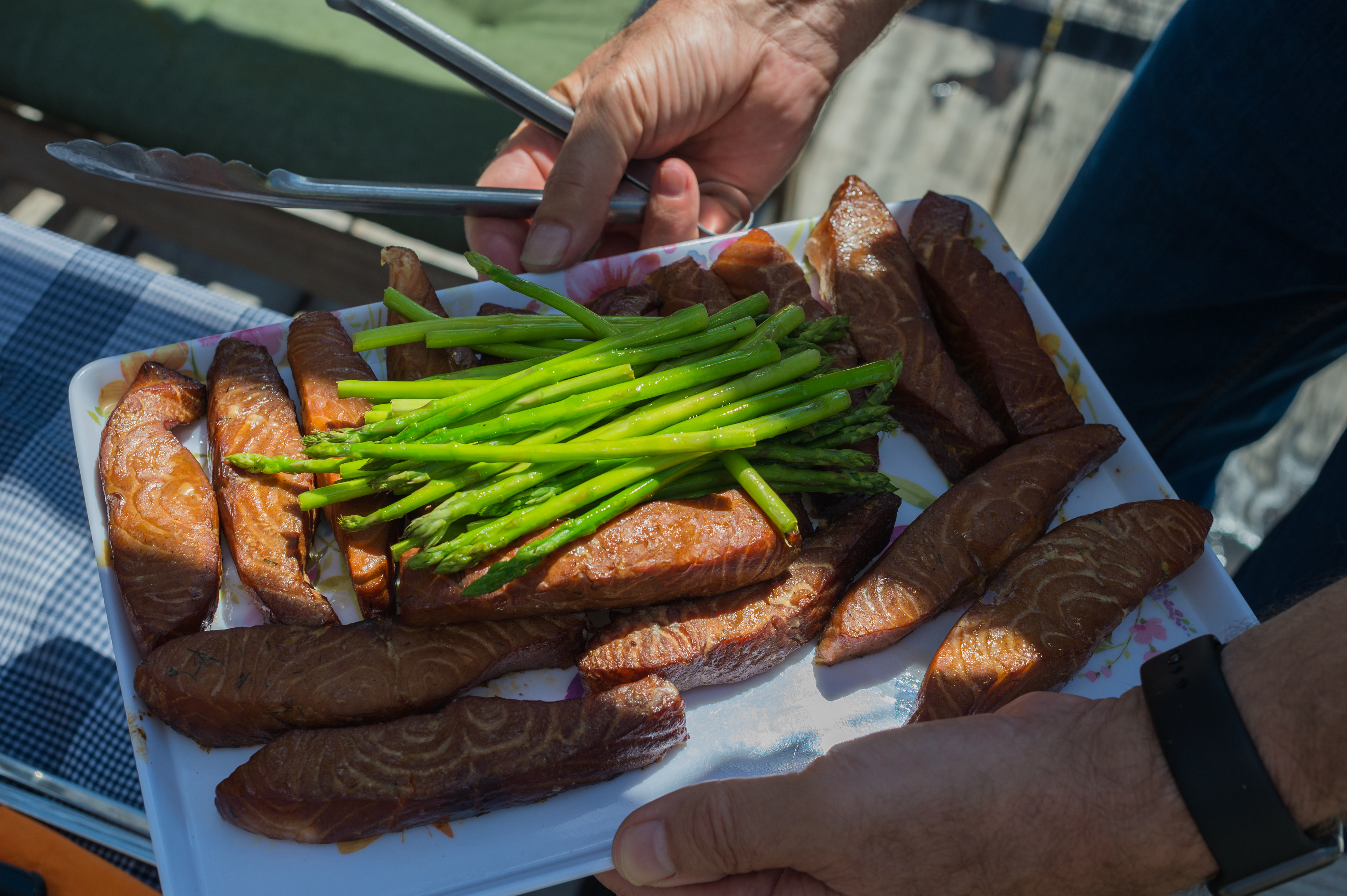 A person holds a plate of grilled salmon and asparagus, using tongs to serve the food.
