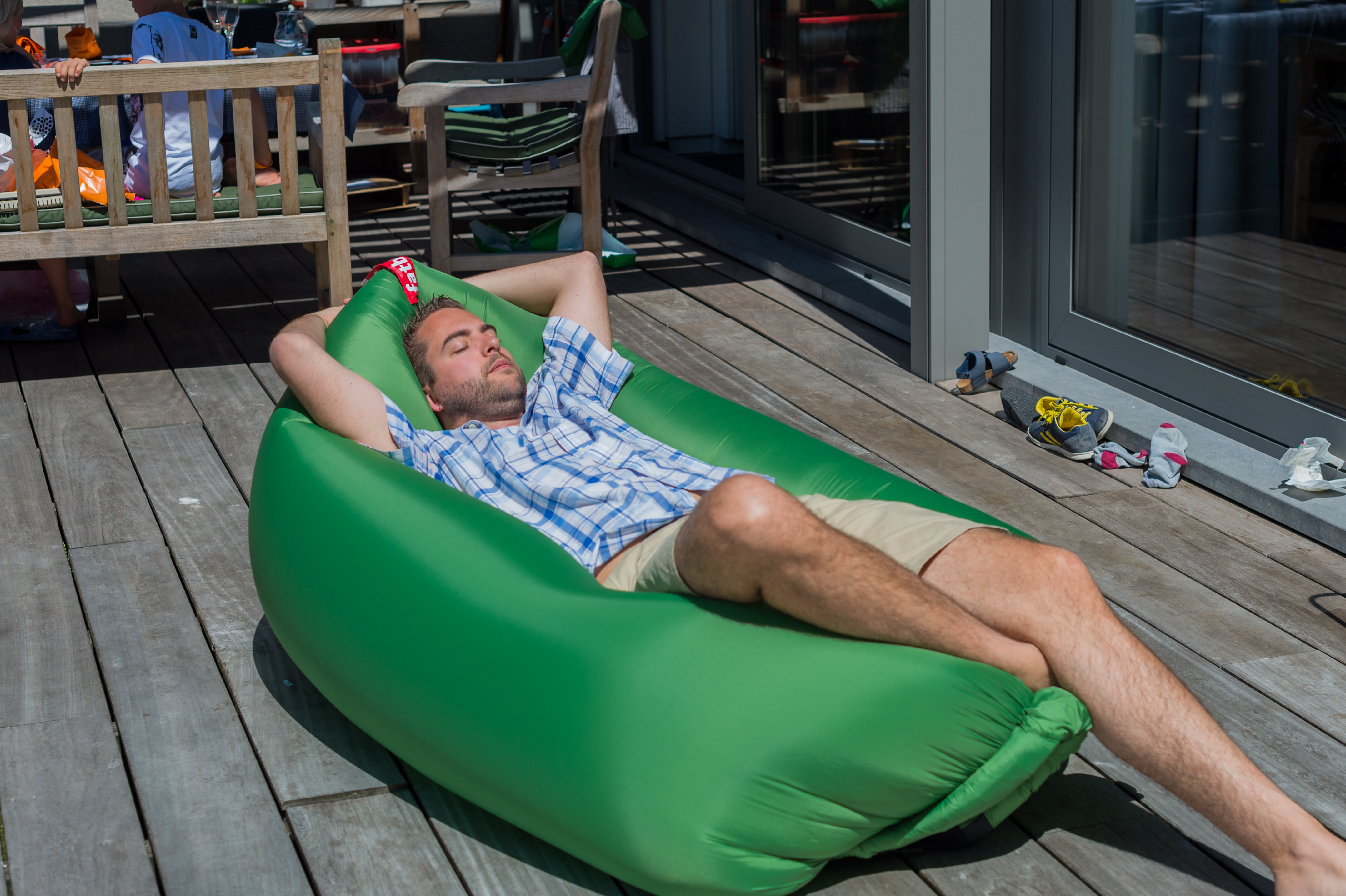A man in a plaid shirt and shorts relaxes on a green inflatable lounger with his eyes closed.