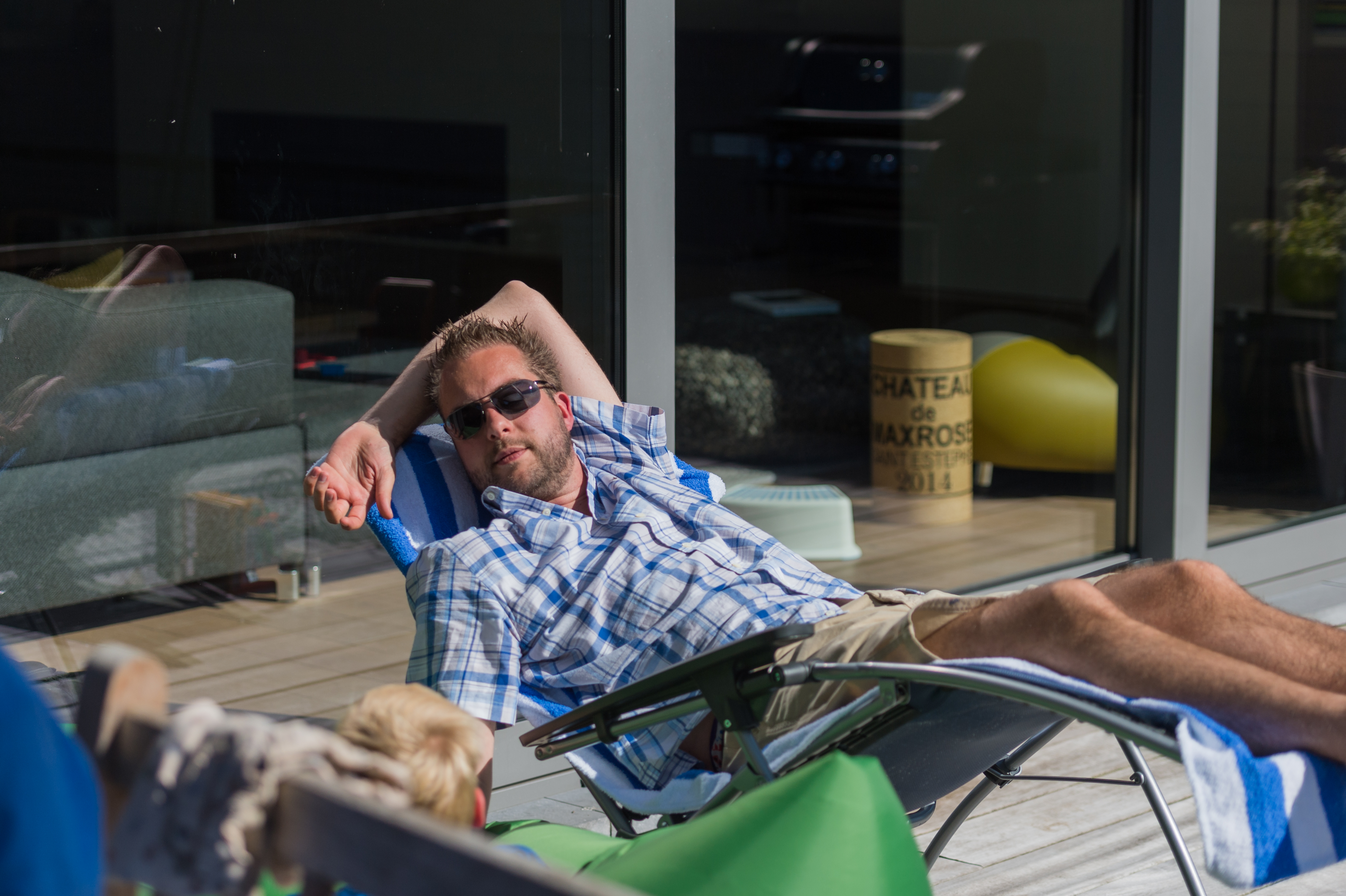 A man wearing sunglasses reclines on a lounge chair outdoors, resting with one arm behind his head.