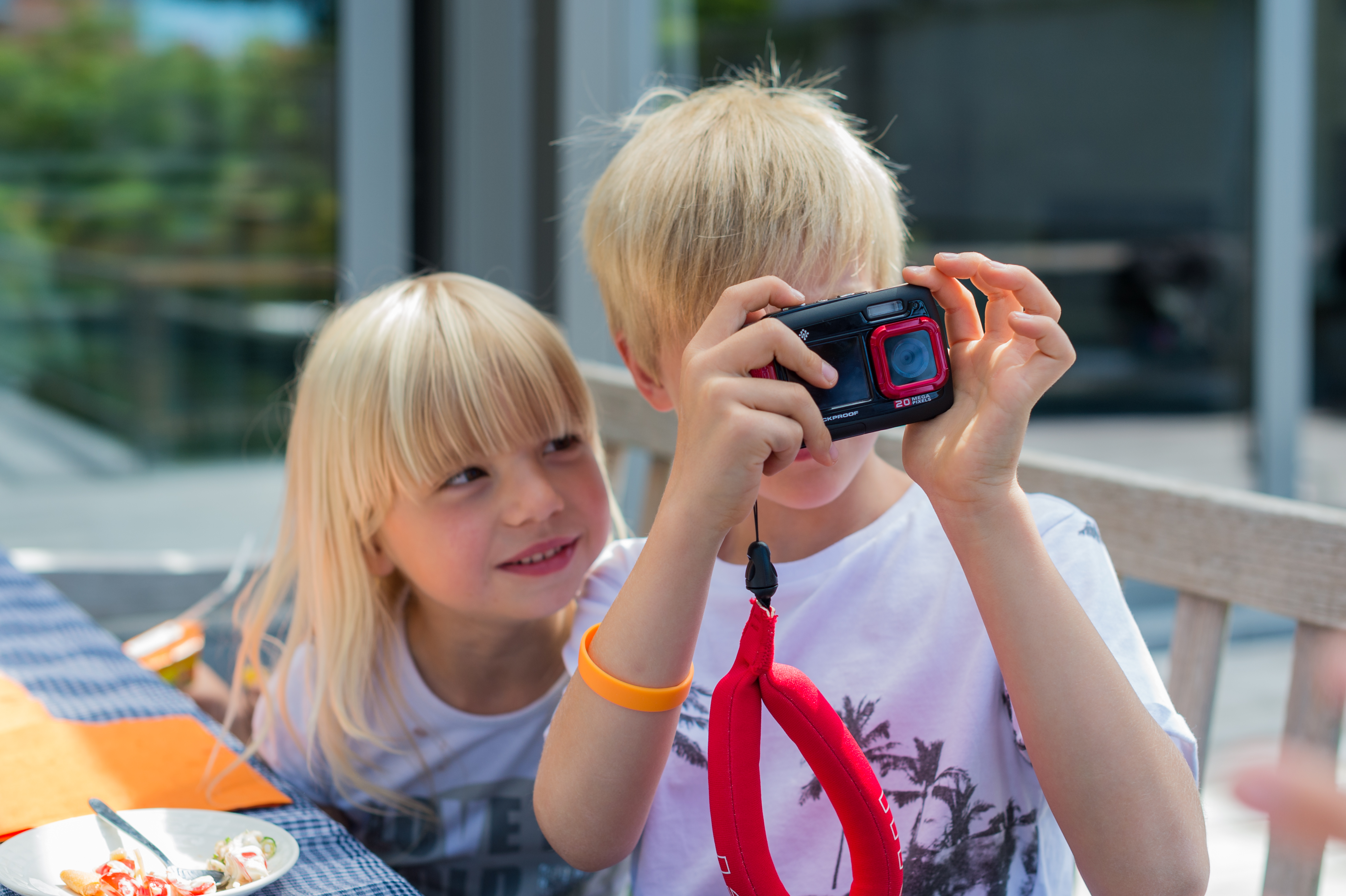 A child holds a camera and takes a photo while another child watches and smiles.