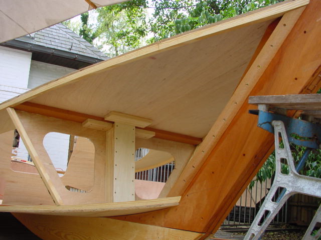 Partially built wooden boat with a sturdy frame, supported by a workbench, in an outdoor workspace.