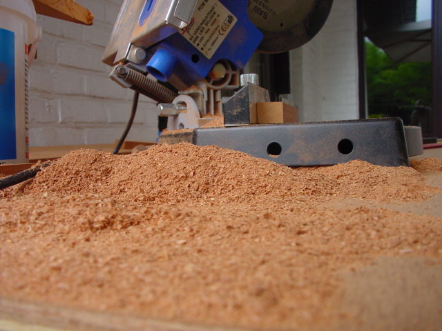 A power saw sits on a workbench surrounded by a large pile of sawdust from recent cutting.