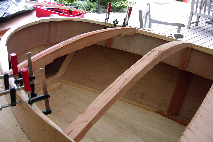 A wooden boat under construction with curved support beams clamped in place.