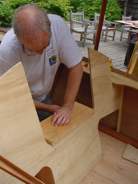 A person assembles a wooden boat, pressing a panel into place with both hands.