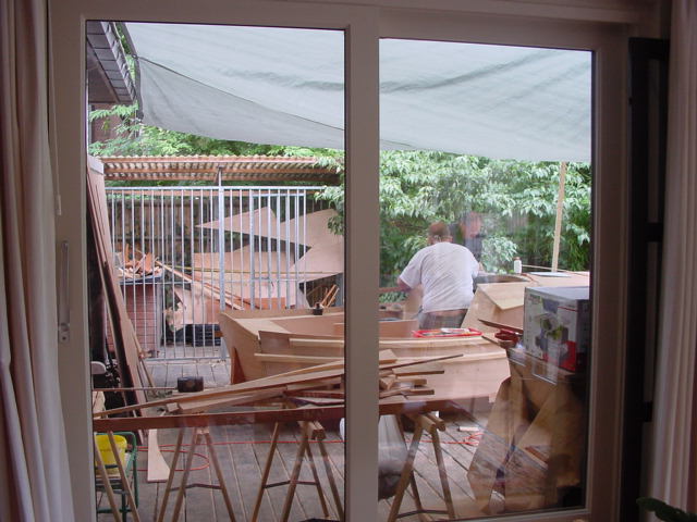 A person is building a wooden boat outdoors, with tools and materials spread across a work area.