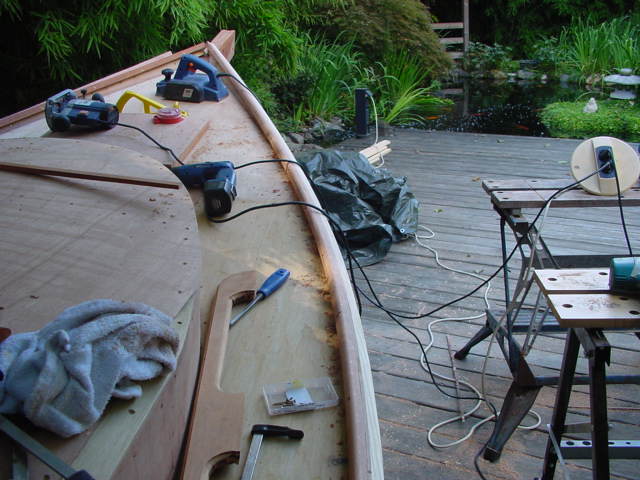 A wooden boat under construction with power tools, clamps, and hand tools on a deck.