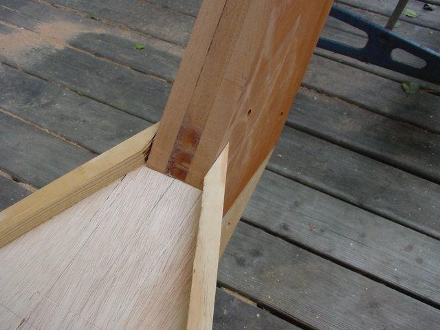 Partially assembled wooden boat frame with joined panels, placed on a wooden deck.