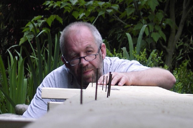 A man carefully inspects a wooden boat frame with nails sticking out, adjusting the alignment.