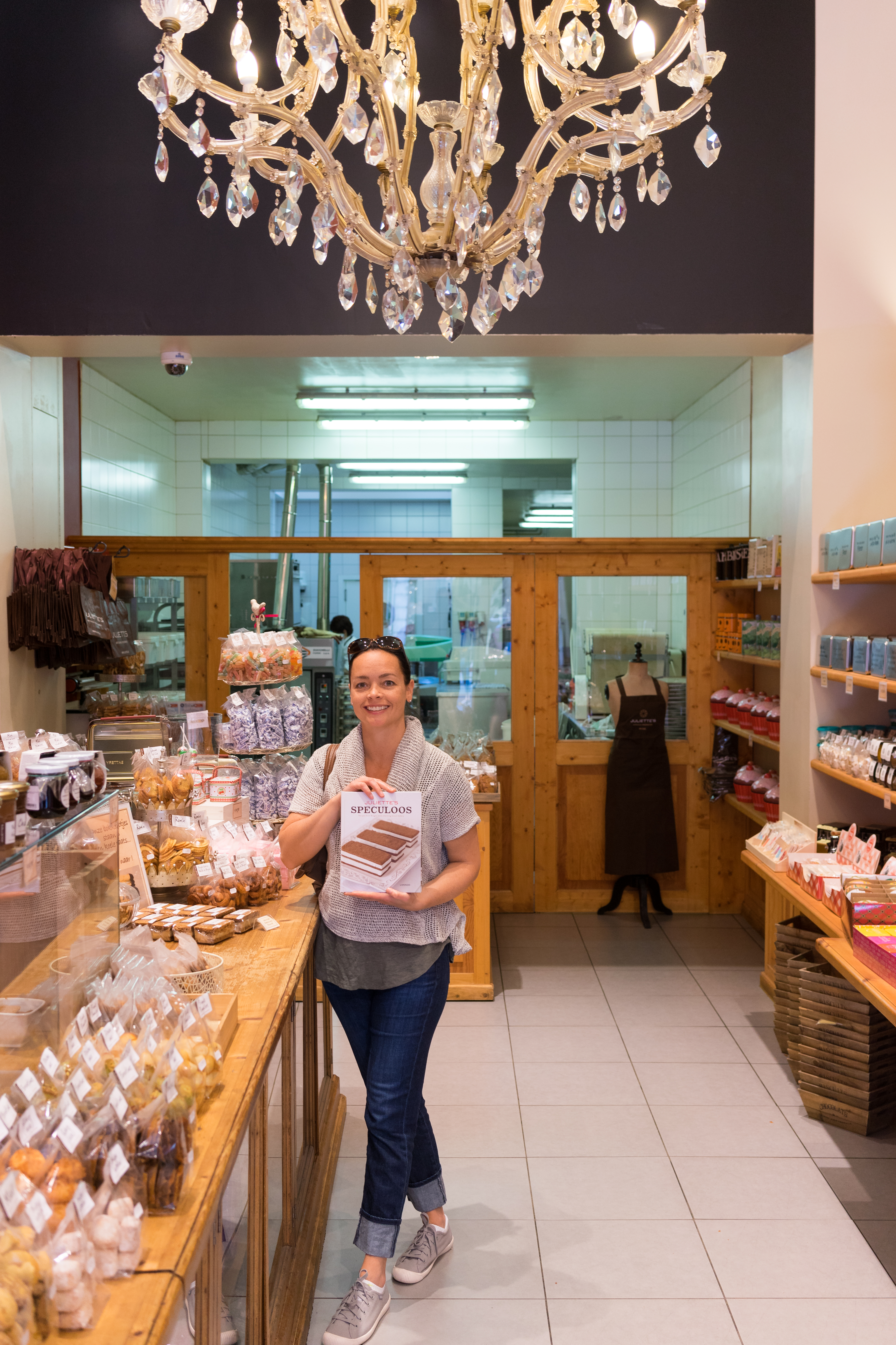 A woman stands in a bakery, smiling and holding a book titled "Speculoos.