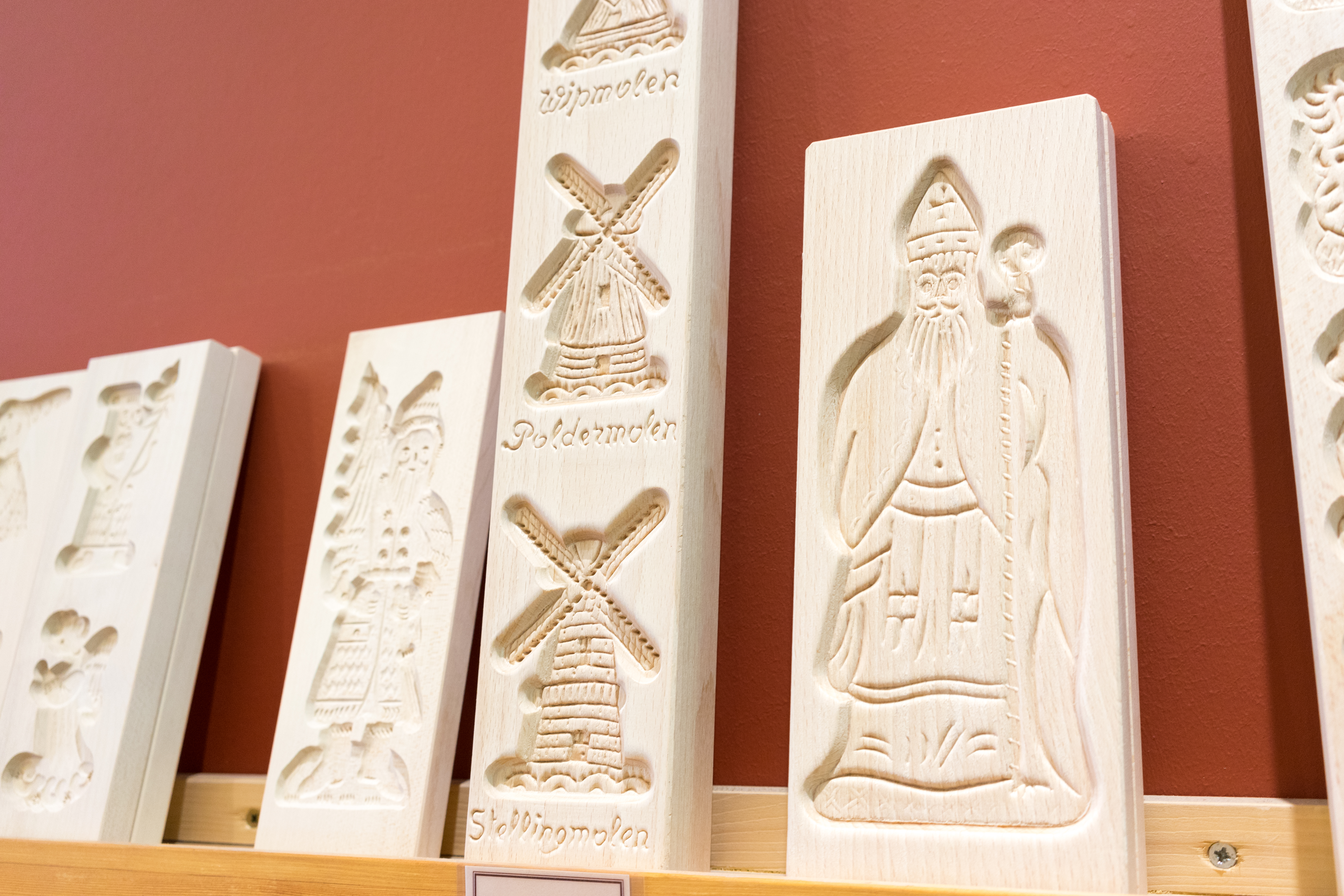Wooden speculoos cookie molds with carved designs of windmills and Saint Nicholas are displayed on a shelf.