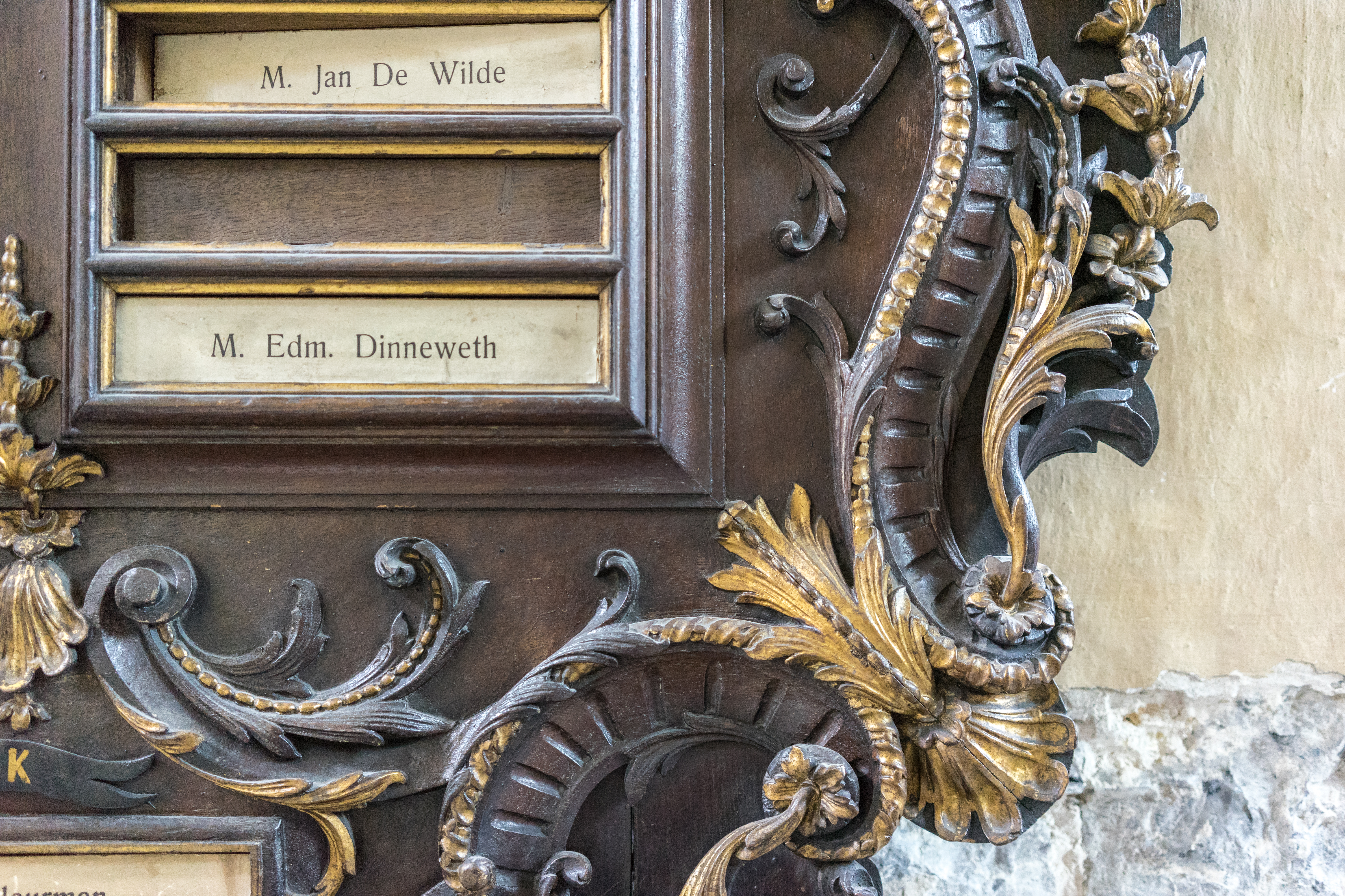 A close-up of an ornate wooden plaque with gold detailing and nameplates inside Our Lady Church in Bruges.