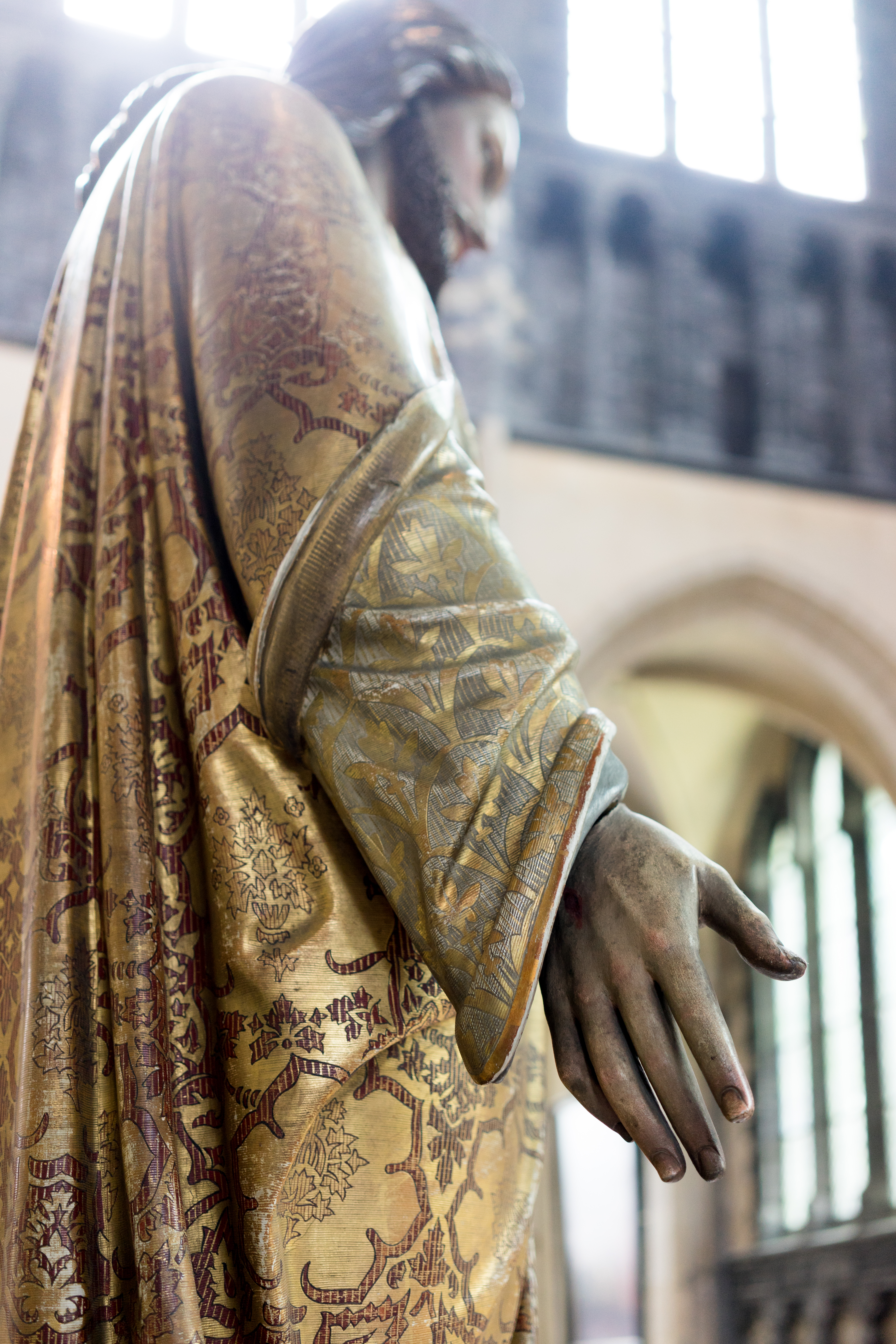 Close-up of a statue in Our Lady Church, showing an outstretched hand and detailed gold-patterned robe.
