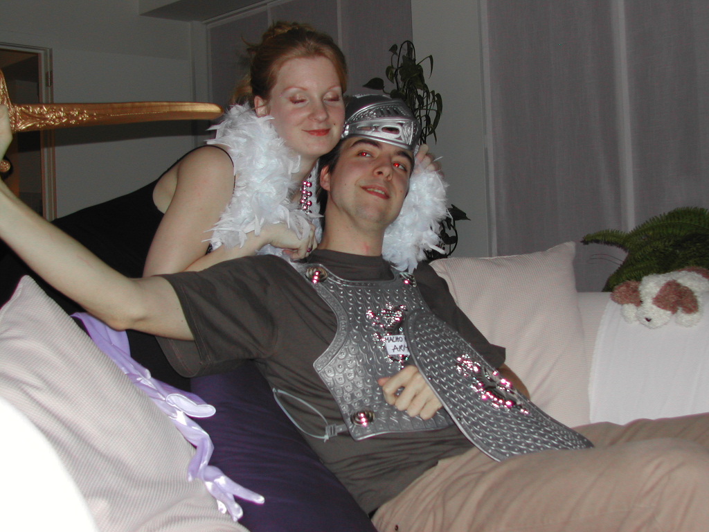 Two people in festive costumes, one dressed as a knight and the other with a feather boa, posing playfully.