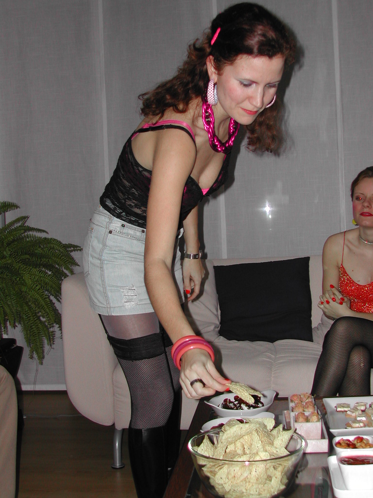 A woman in a festive outfit reaches for food from a table with snacks at a gathering.