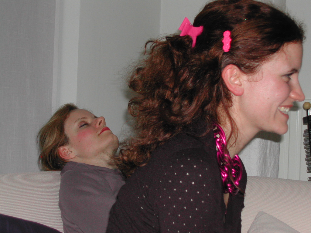 A woman with festive accessories smiles while another person leans back on a couch with closed eyes.