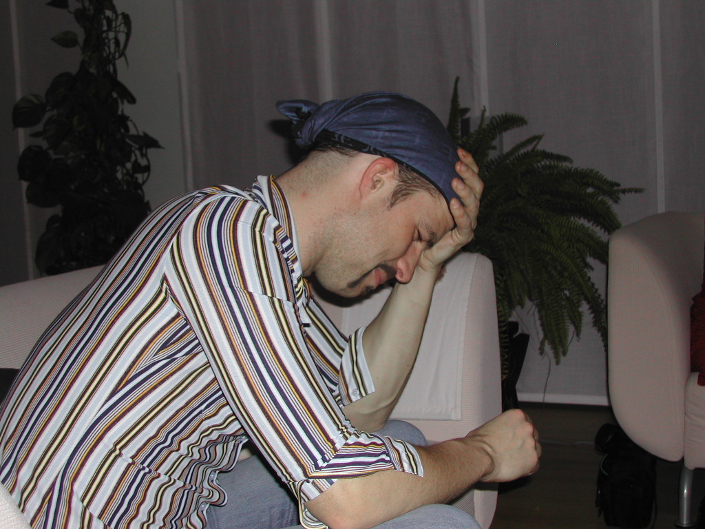 A man in a striped shirt sits with his head in his hand, appearing tired or unwell.