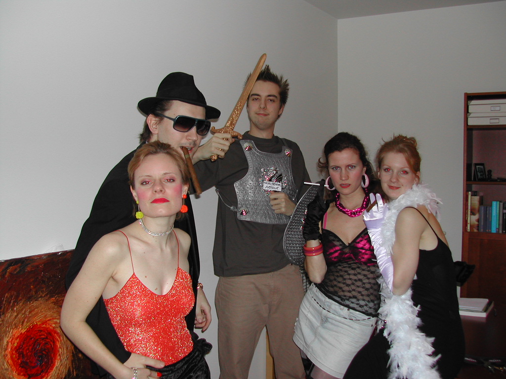 Five people in colorful costumes pose together indoors, dressed for a carnival celebration with accessories and props.