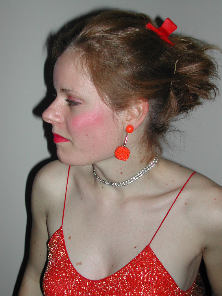 A woman in a red sparkly dress with matching accessories looks to the side during a carnival event.