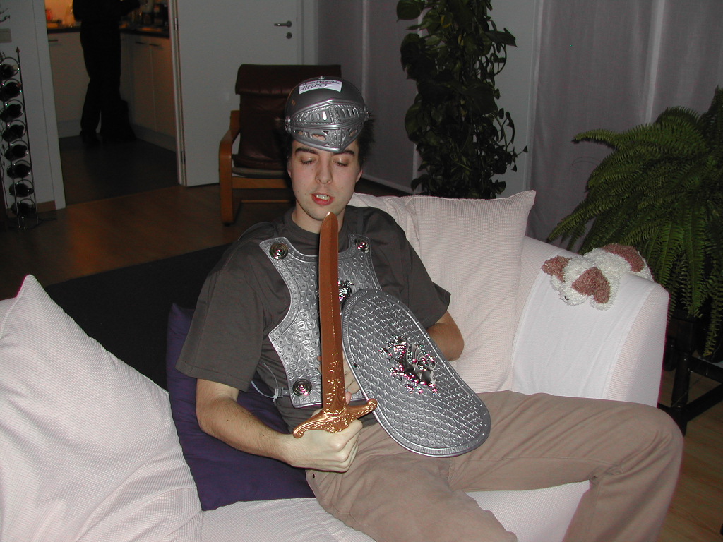 A person in a toy knight costume sits on a couch, holding a plastic sword and shield.
