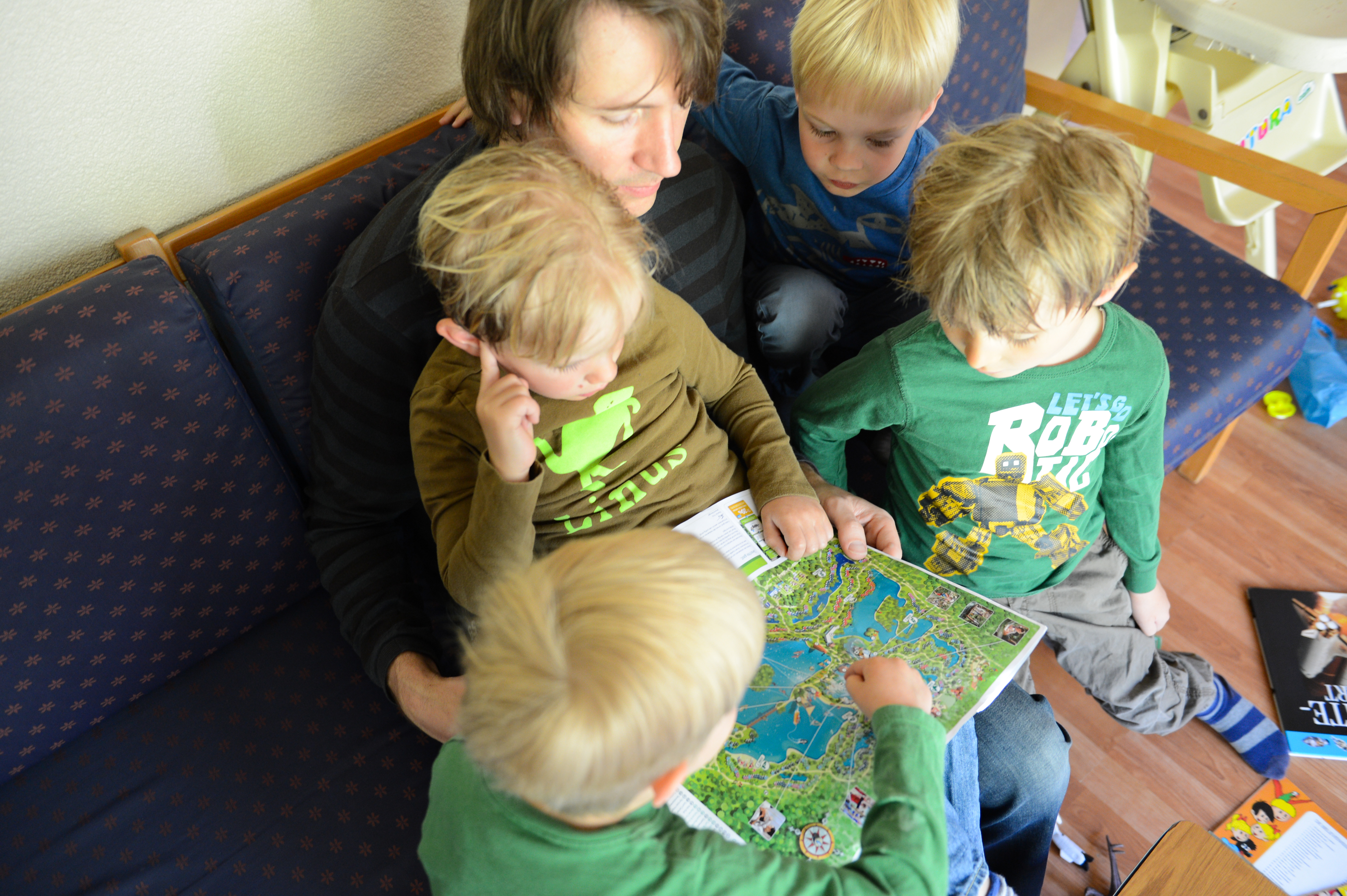 An adult and four children sit on a couch, looking at and pointing to a detailed map together.
