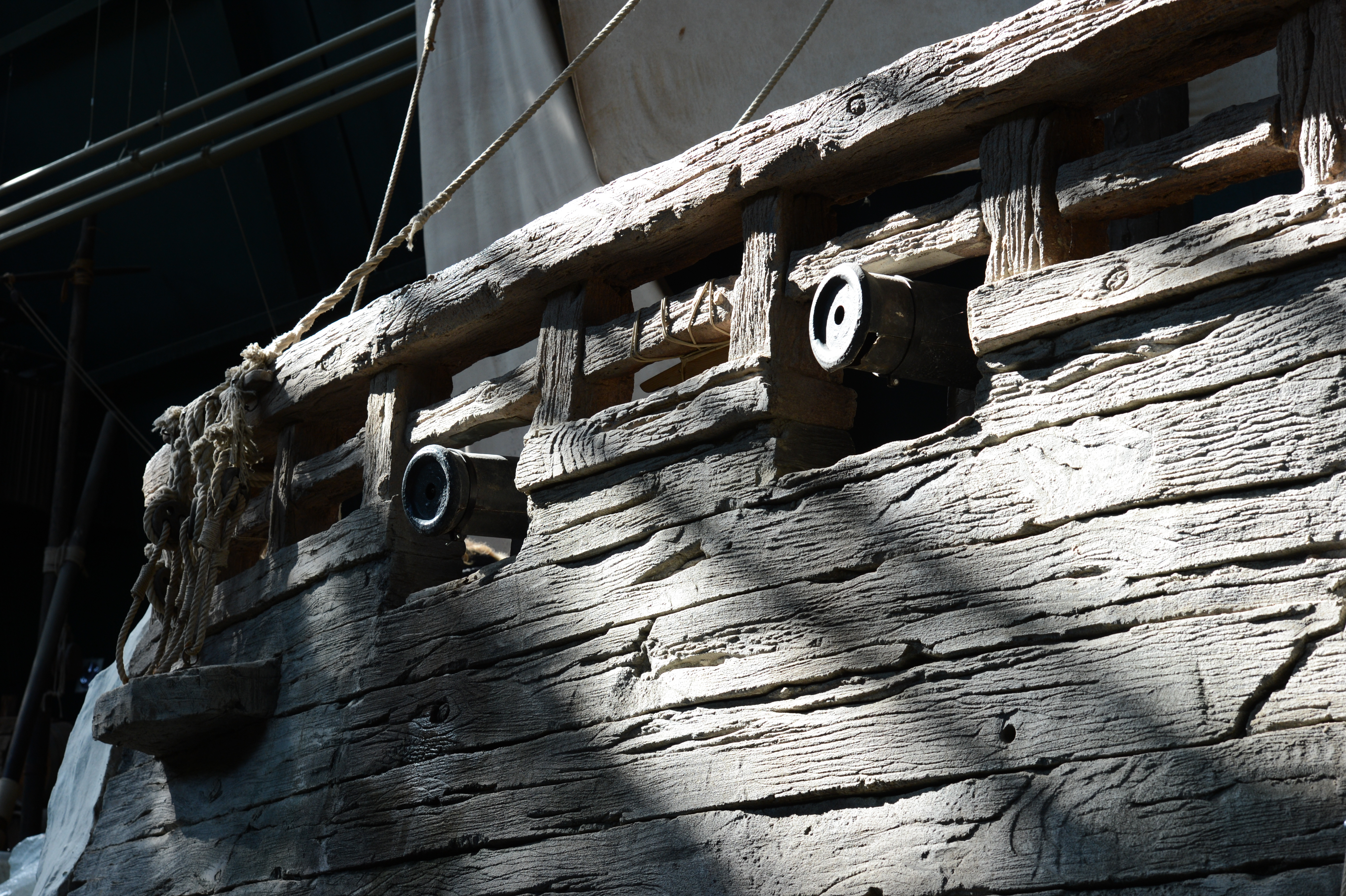 Close-up of a wooden ship replica with small cannons sticking out from the sides, illuminated by sunlight.