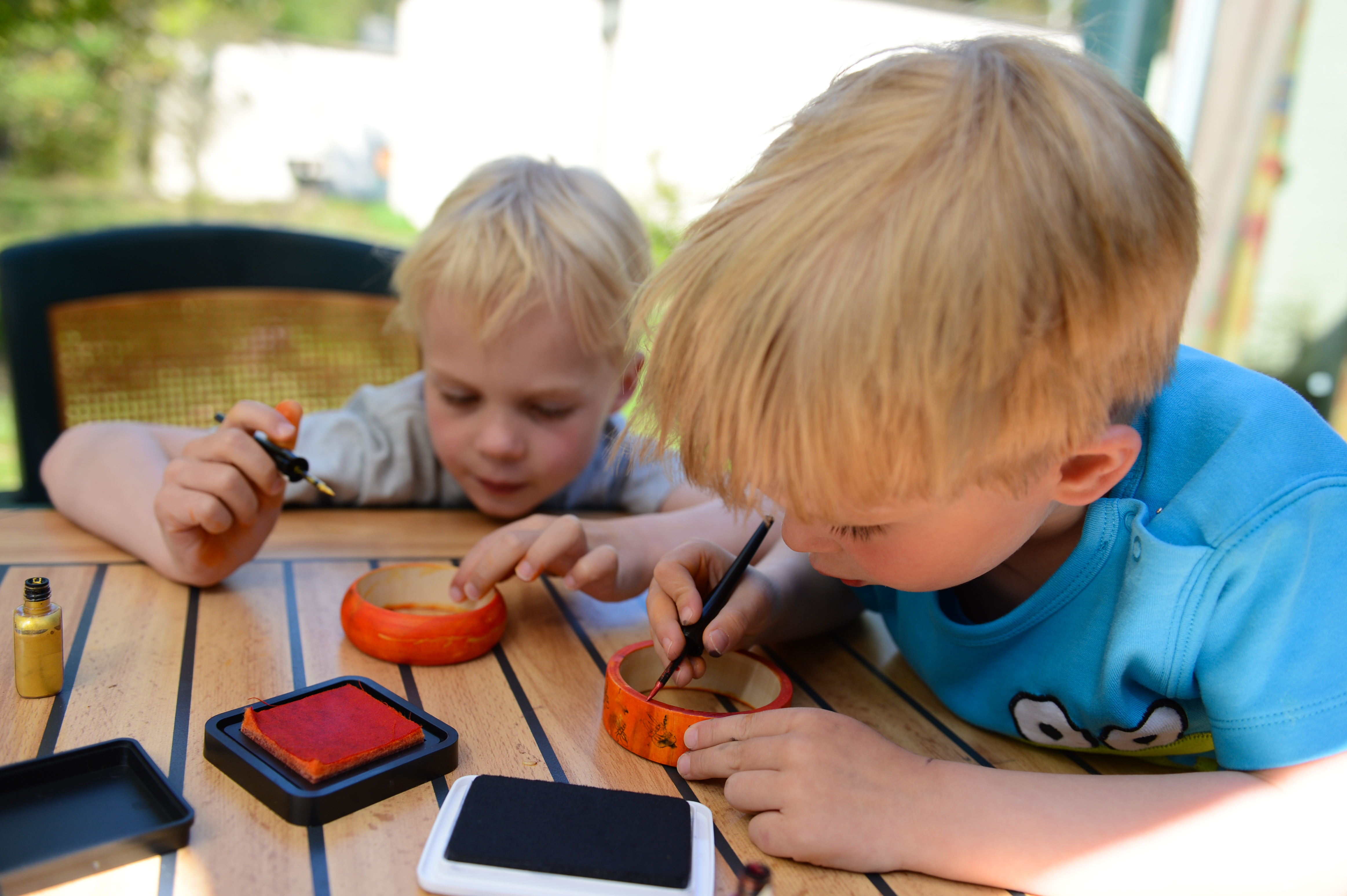 Two young children sit at a wooden table, carefully painting small bowls with brushes and ink.