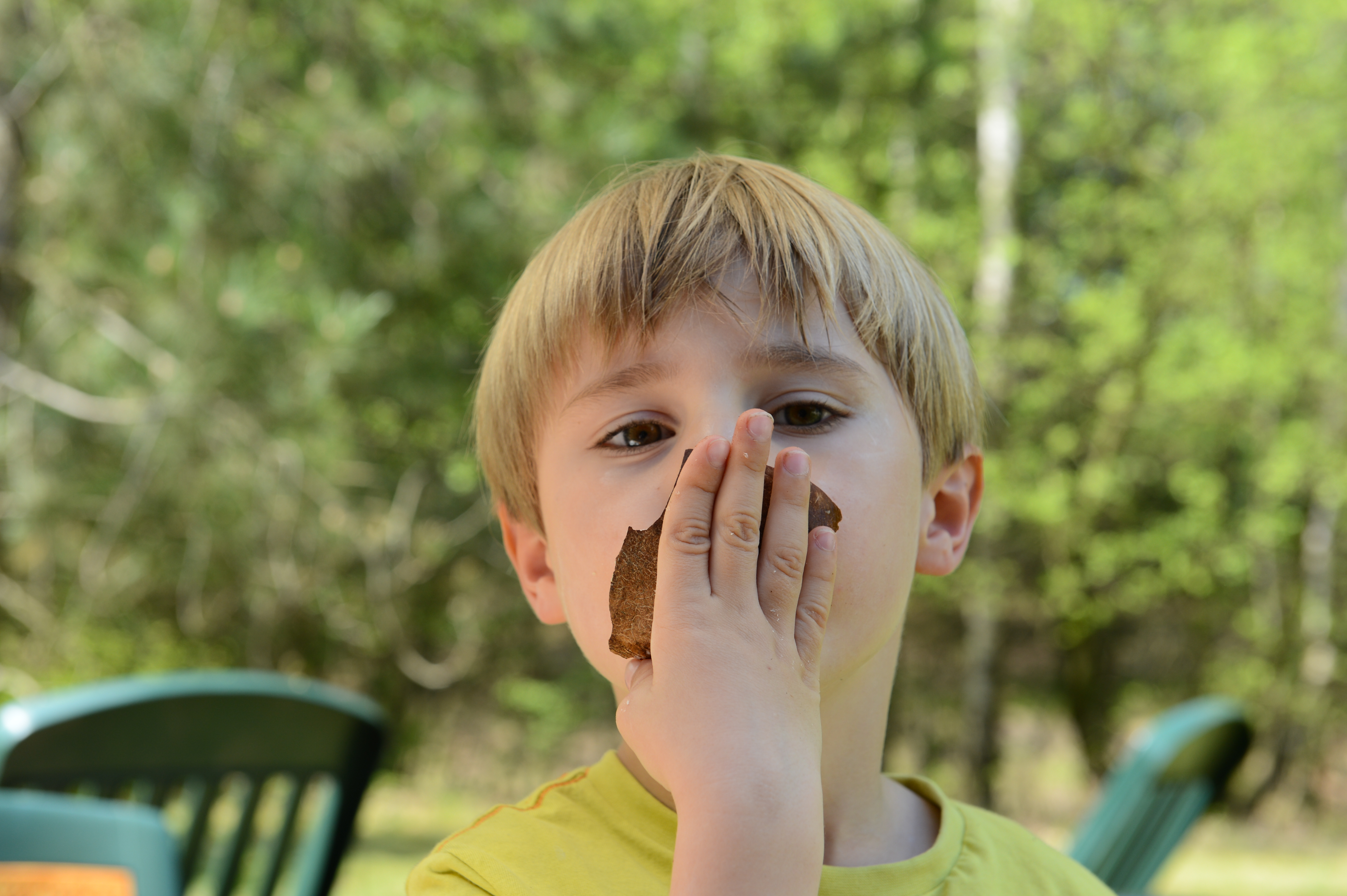 A young child in a yellow shirt holds a piece of food to their mouth while looking at the camera.