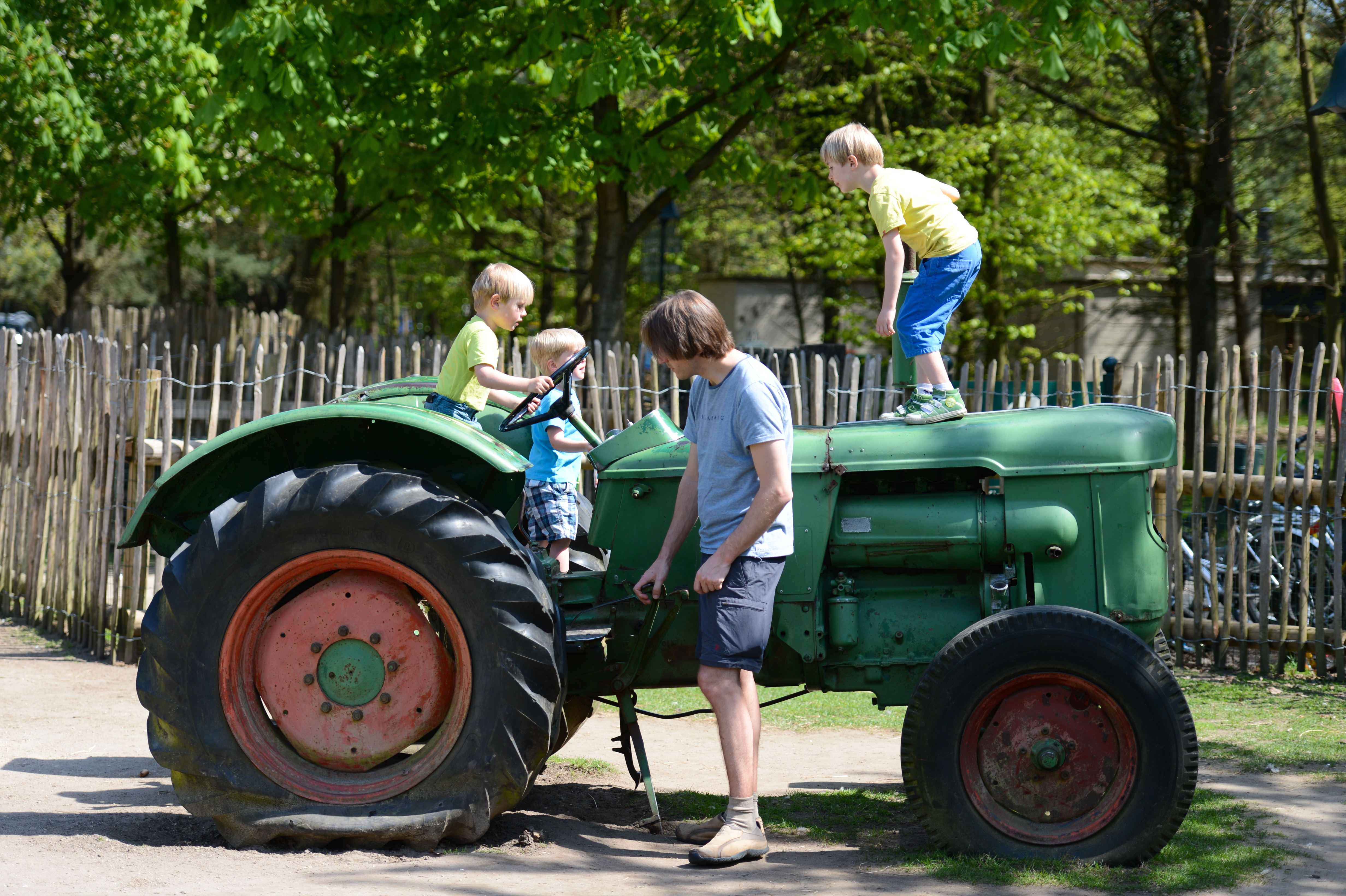 An adult helps children climb and play on an old green tractor in an outdoor setting.