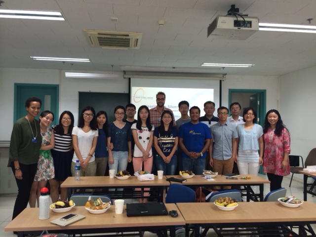 A group of students and faculty pose for a photo in a university classroom with food on tables.