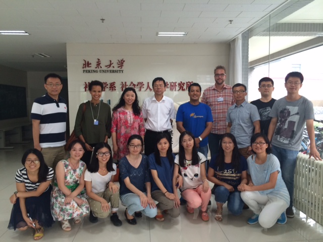 A group of students and faculty pose for a photo inside Peking University, standing and kneeling in two rows.