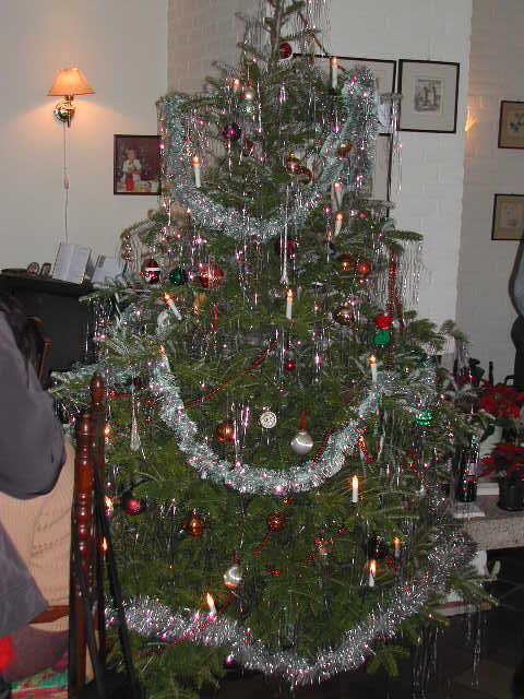A decorated Christmas tree with tinsel, ornaments, and candles stands in a living room.