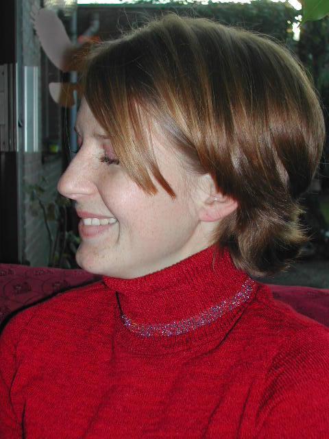 A person wearing a red turtleneck sweater smiles while looking to the side.