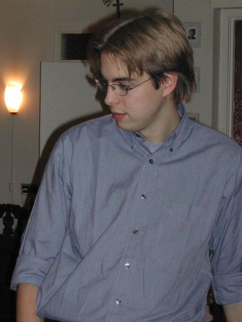 A young man in glasses and a blue shirt looks to the side in an indoor setting.