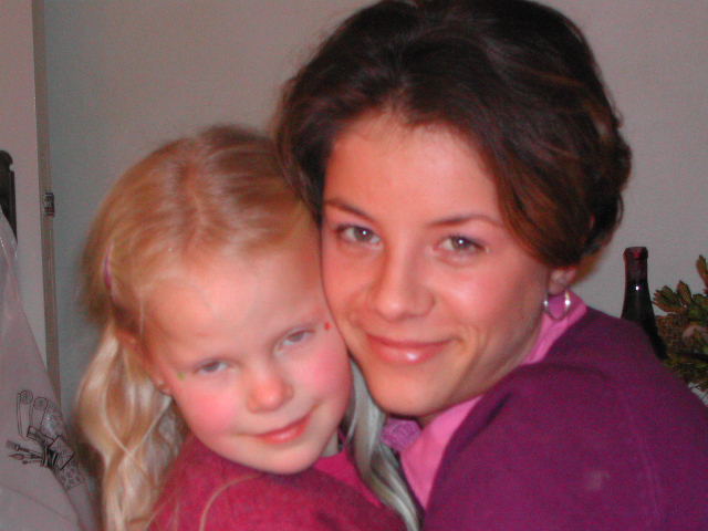 Two people wearing pink and purple clothing share a close hug and smile at the camera.