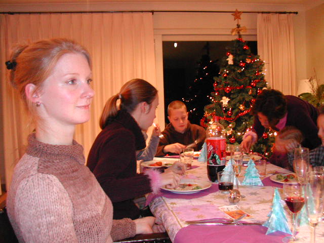 Family gathered around a table enjoying a Christmas meal, with a decorated tree in the background.