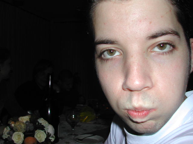 A person in a white shirt is close to the camera, making a playful facial expression at a holiday gathering.