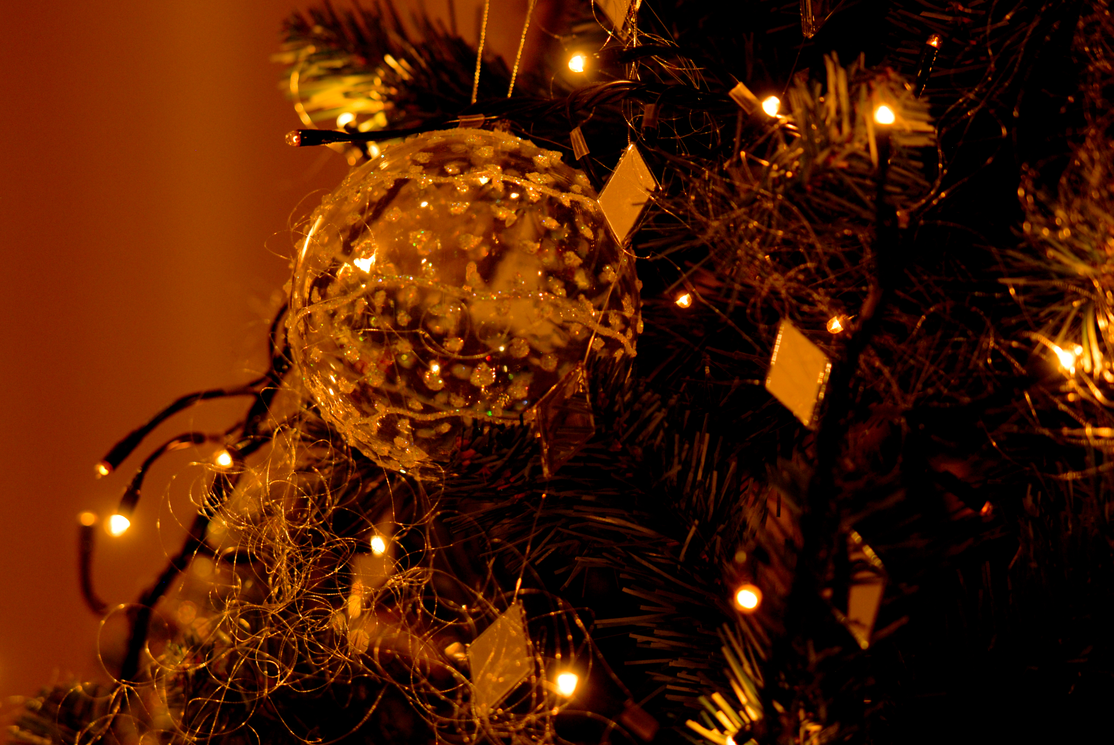 A decorated Christmas tree with glowing lights and a clear ornament hanging among the branches.