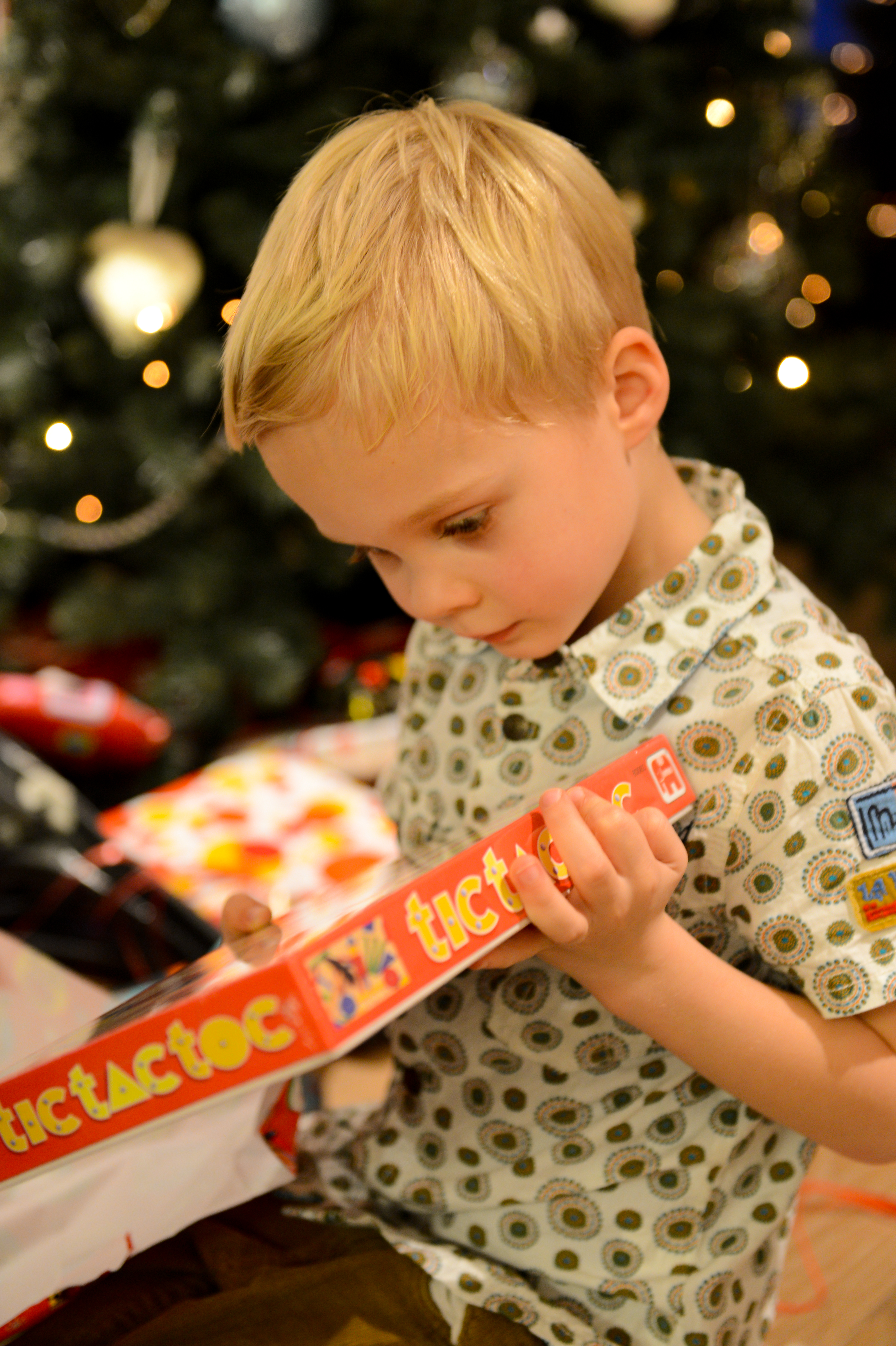 A young child unwraps a board game gift, looking at it with focus.