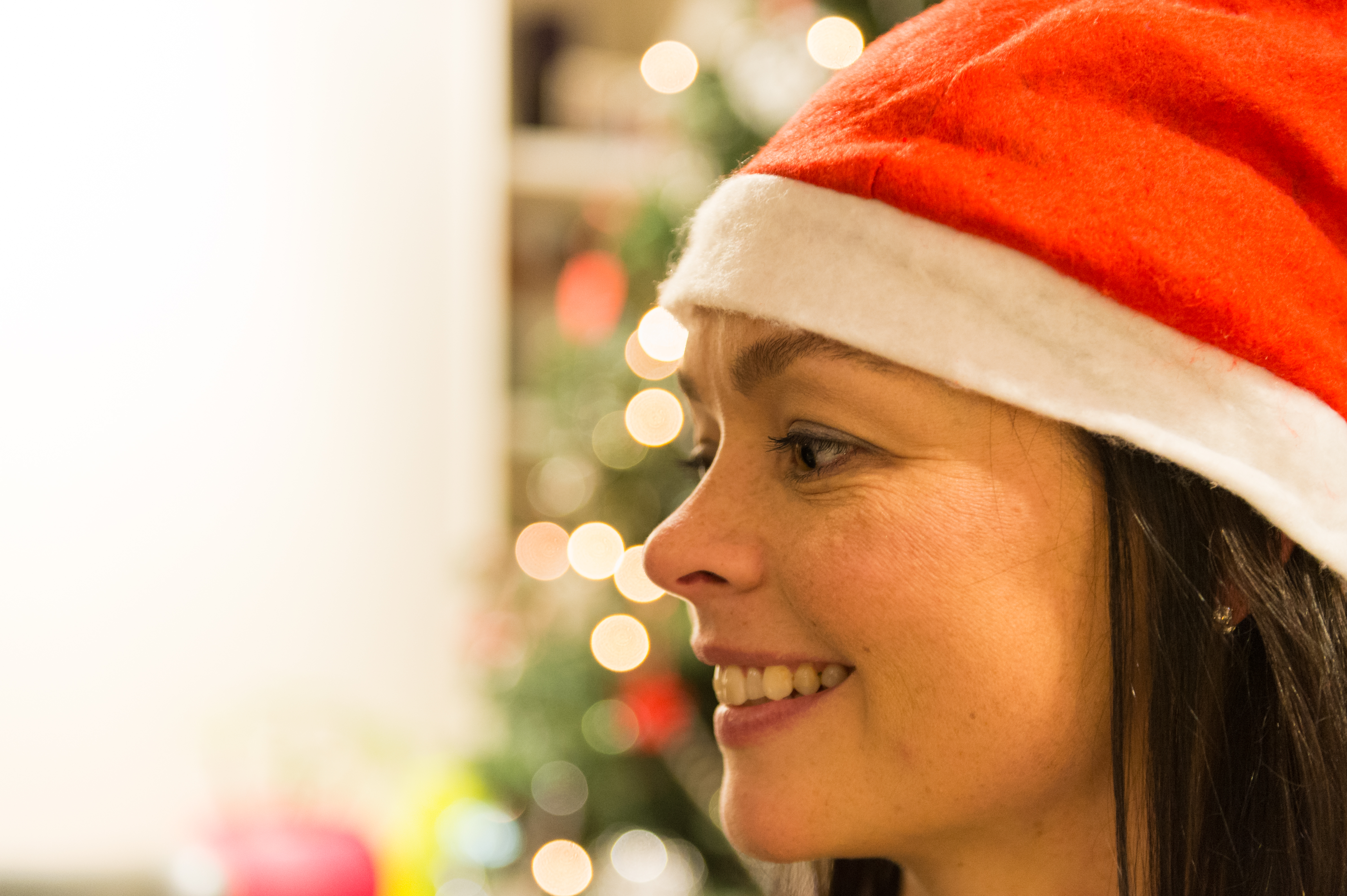 A person wearing a Santa hat smiles, with a decorated Christmas tree in the blurred background.