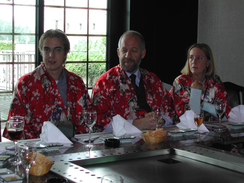 Three people wearing red floral robes sit at a table with drinks and folded napkins, engaged in conversation.