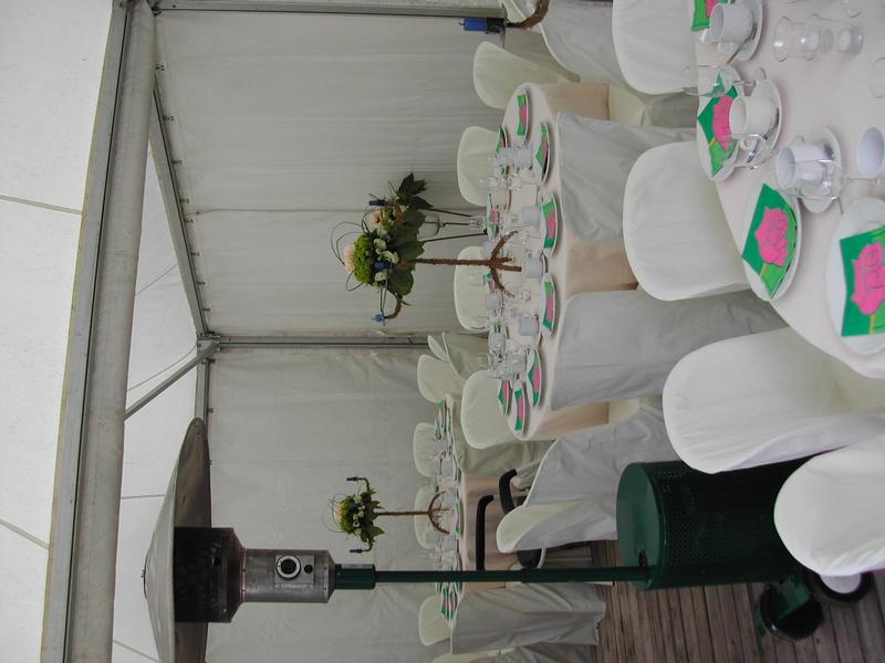 A decorated tent with round tables covered in white cloth, set for a communion party with floral centerpieces.
